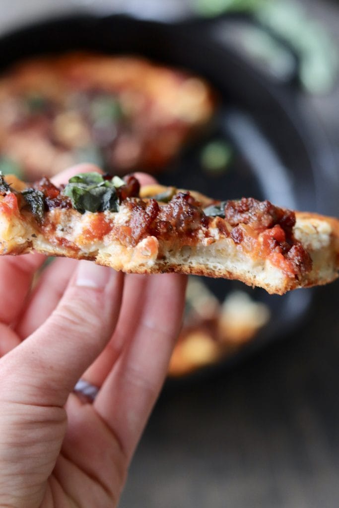 A hand holding a piece of pizza.